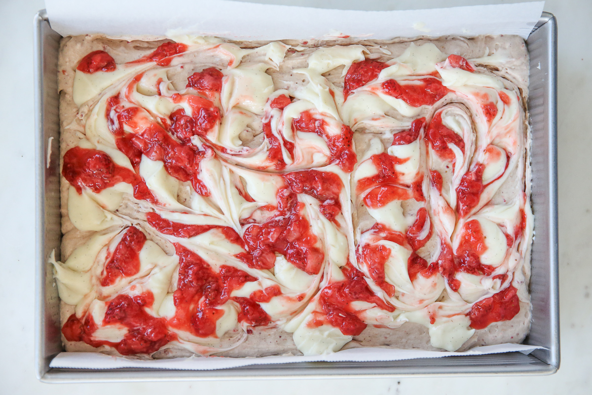 cake batter in a cake pan with cheesecake batter and berry compote swirled in