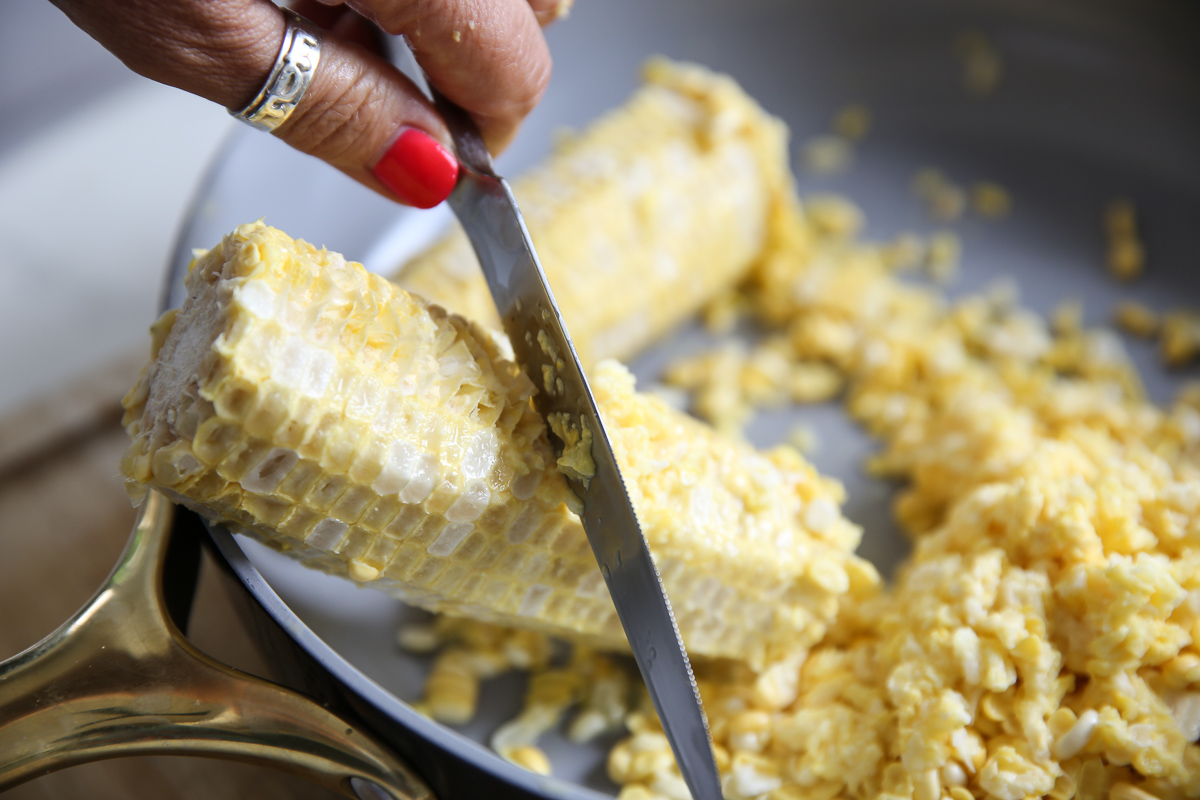 scraping pulp from corn on the cob into the pan