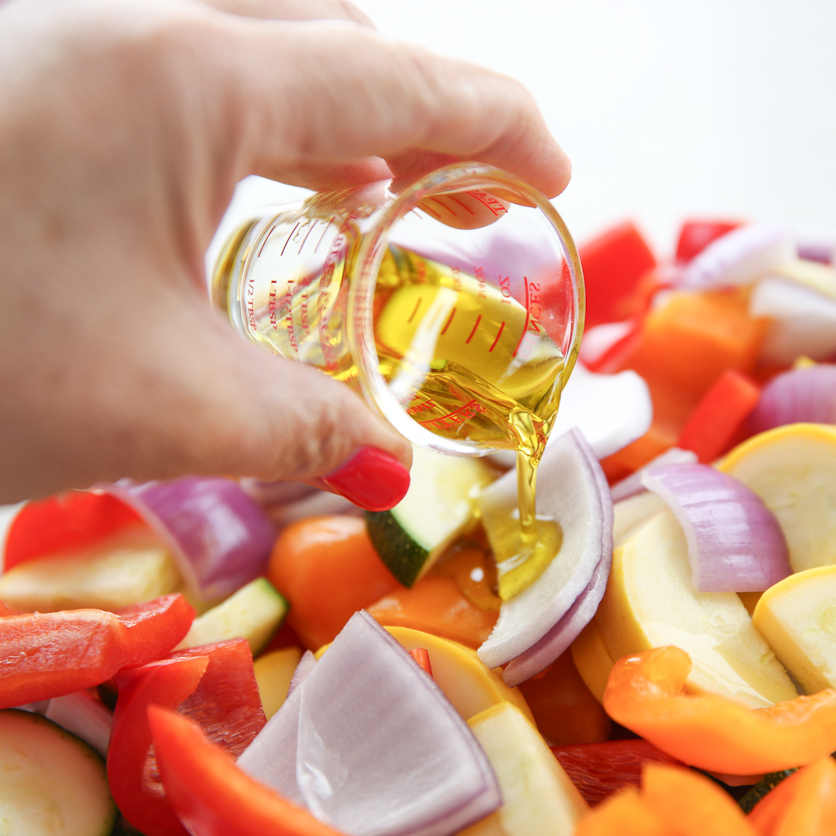 pouring oil over chopped vegetables in a glass bowl