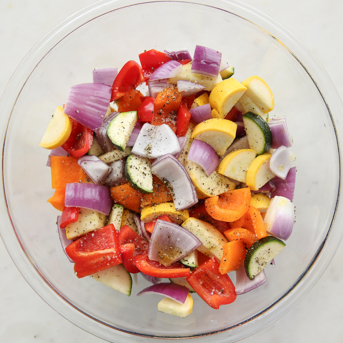 chopped vegetables in a glass bowl with oil, salt and pepper
